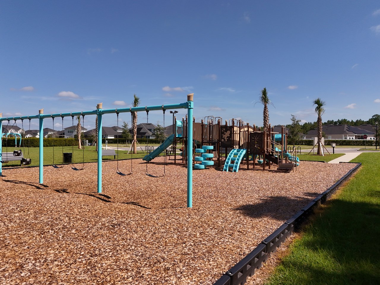 Neighborhood playground with turquoise swings and slides on a wood-chip play area.