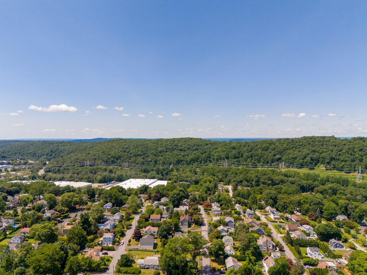 Aerial view of homes among trees, with wooded hills and utility lines in the distance.