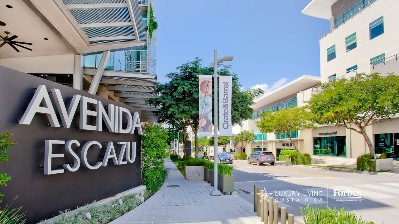 Avenida Escazú streetscape with its large entrance sign, modern storefronts, and tree-lined sidewalk.