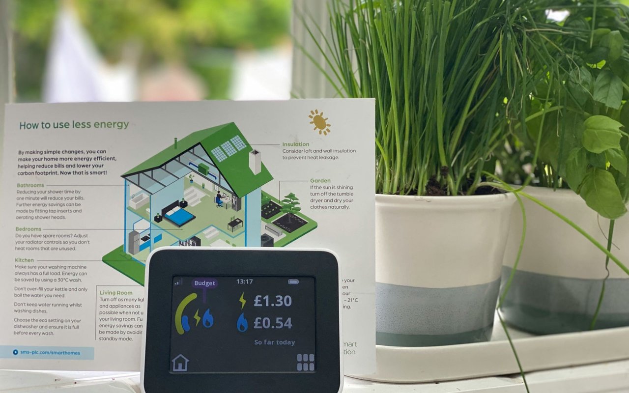 Home energy monitor beside an energy-saving guide and leafy potted plant.