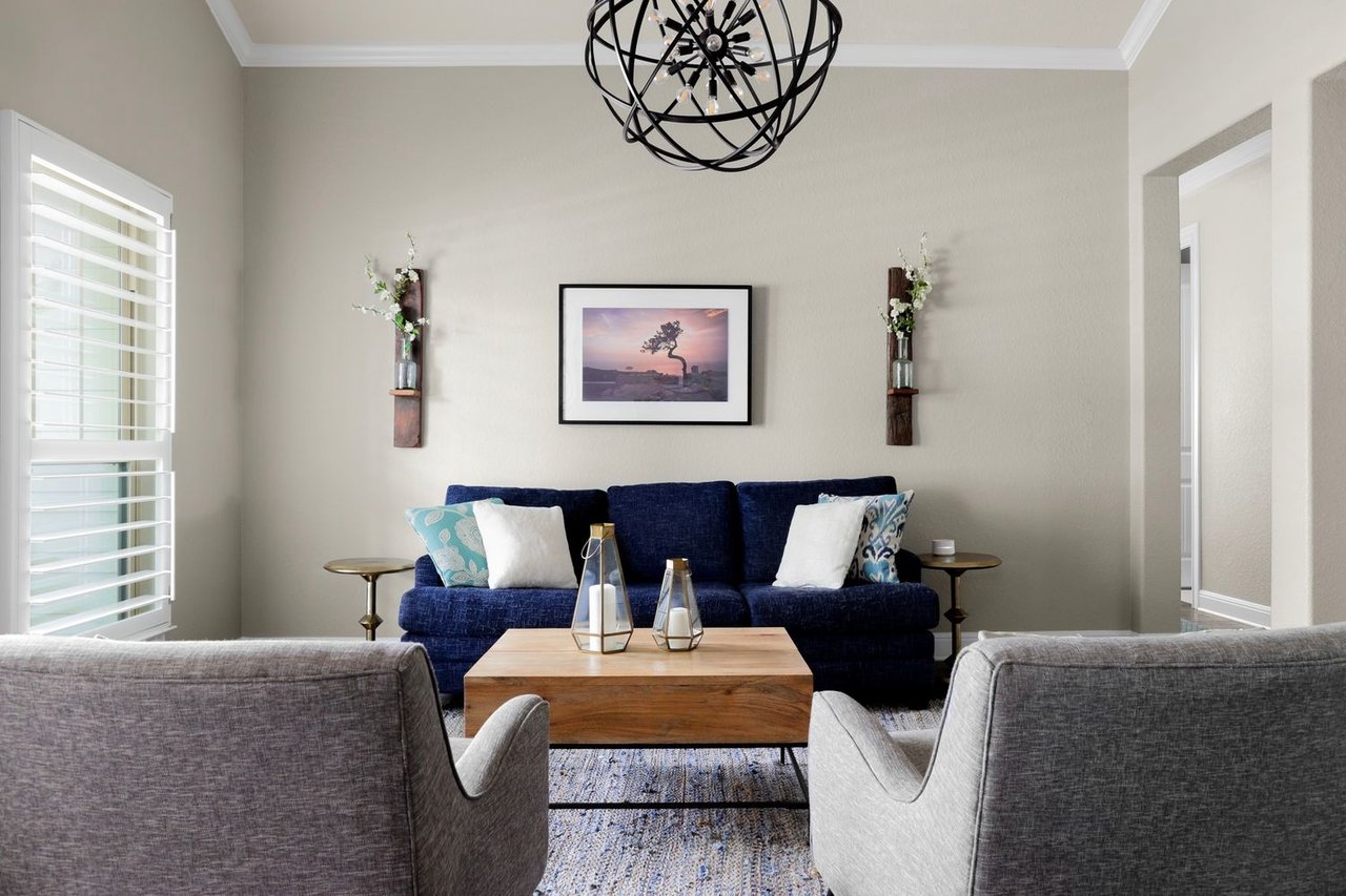 Living room with a navy sofa, gray armchairs, wooden coffee table, and white plantation shutters.