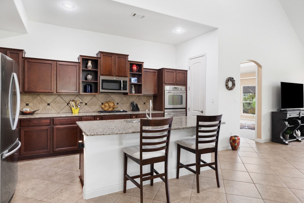 Kitchen with cherry cabinets, stainless steel appliances, and a granite island with two bar stools.