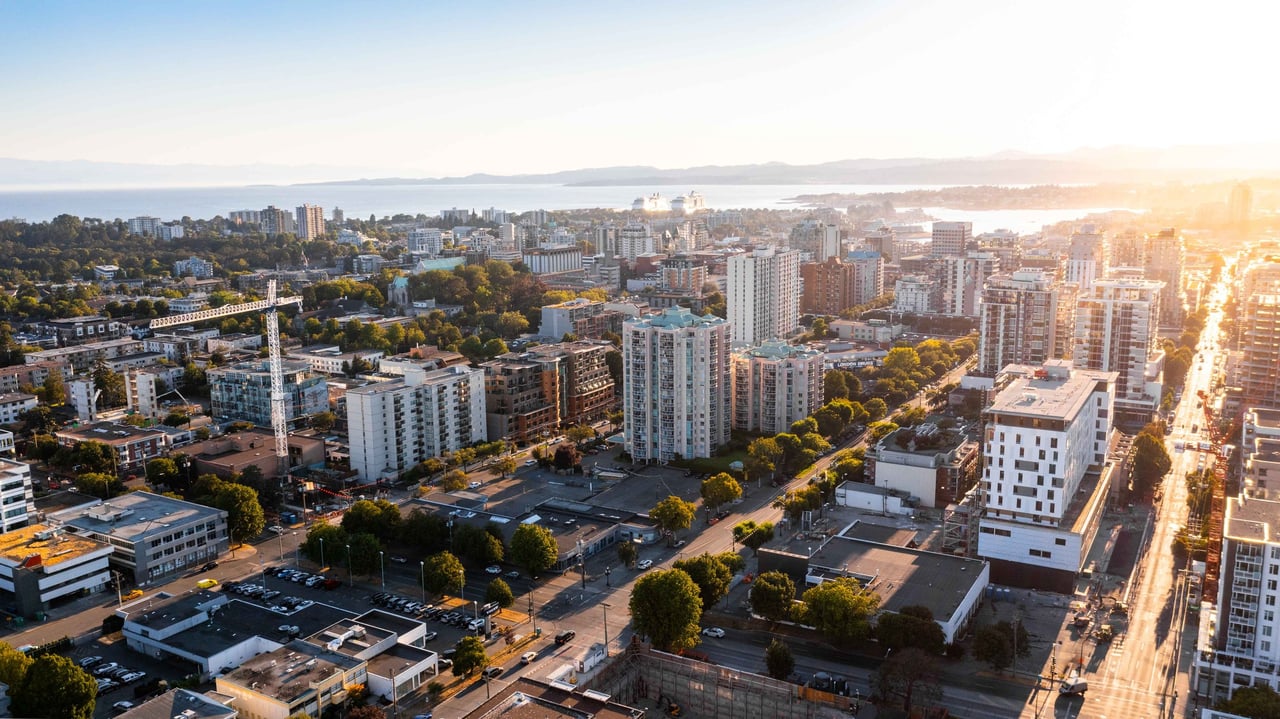 An aerial view of a serene residential neighborhood in Victoria, BC, showcasing modern homes with swimming pools and tree-lined streets, highlighting the appeal of coastal living.