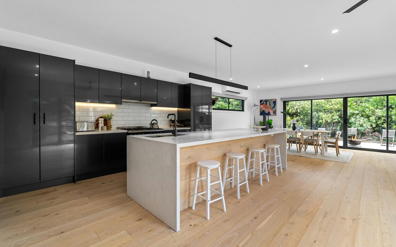 Modern kitchen with black cabinets, a large island, and dining area opening to a garden.