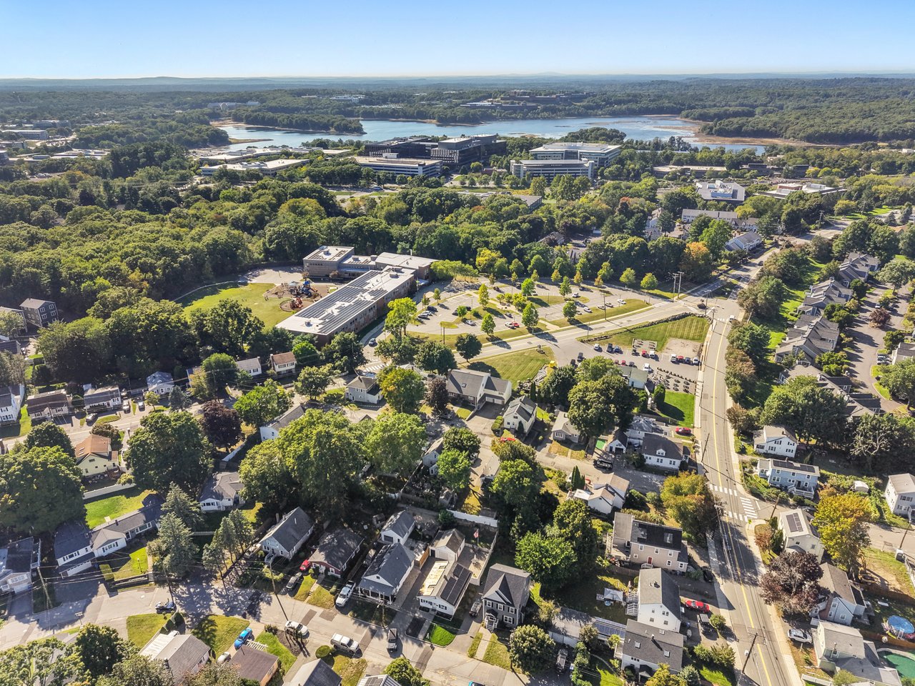 Aerial view of a suburban neighborhood, with a school campus and lake beyond the homes.