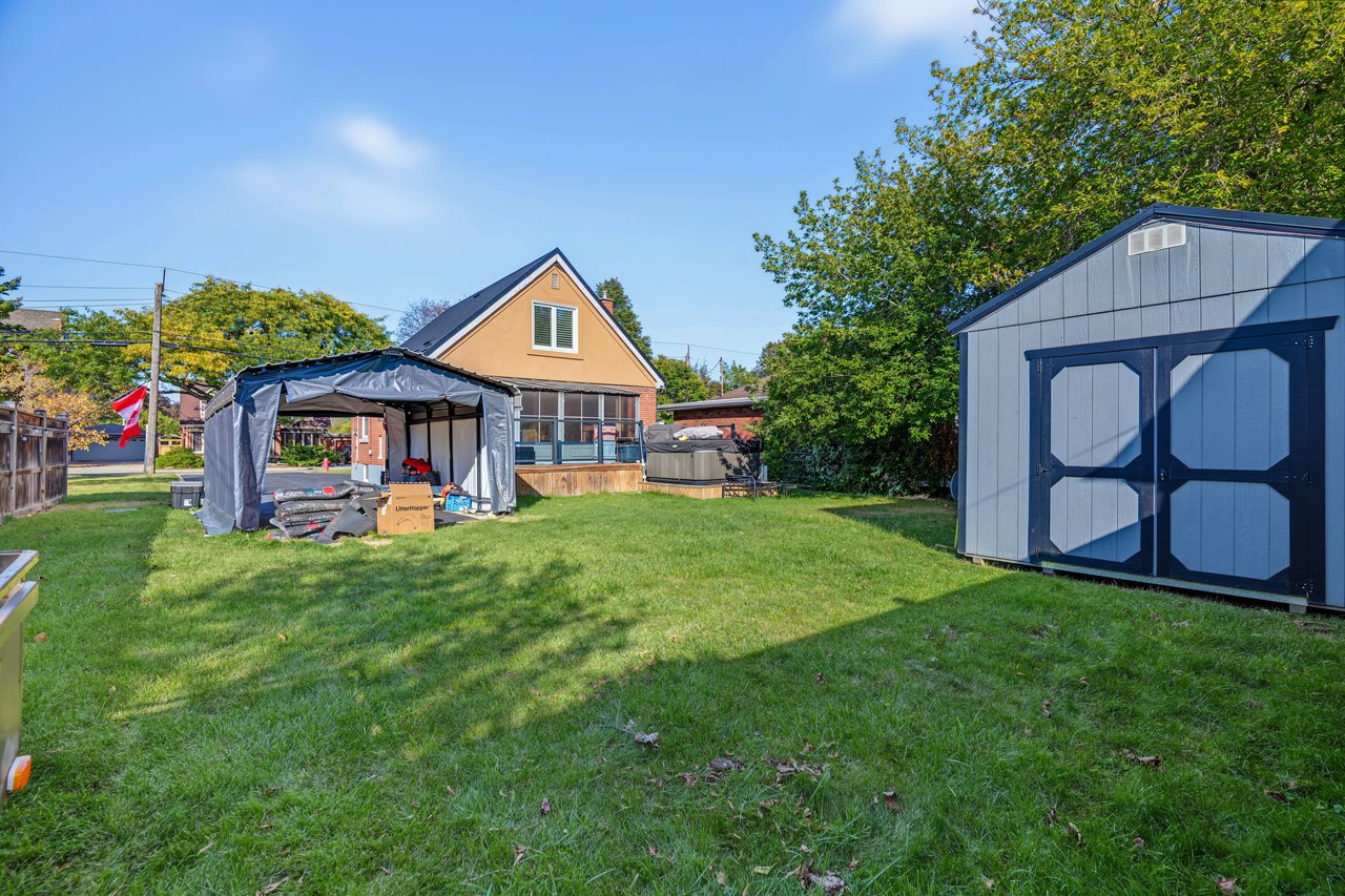 Backyard with a broad lawn, covered canopy, hot tub, and large blue storage shed.