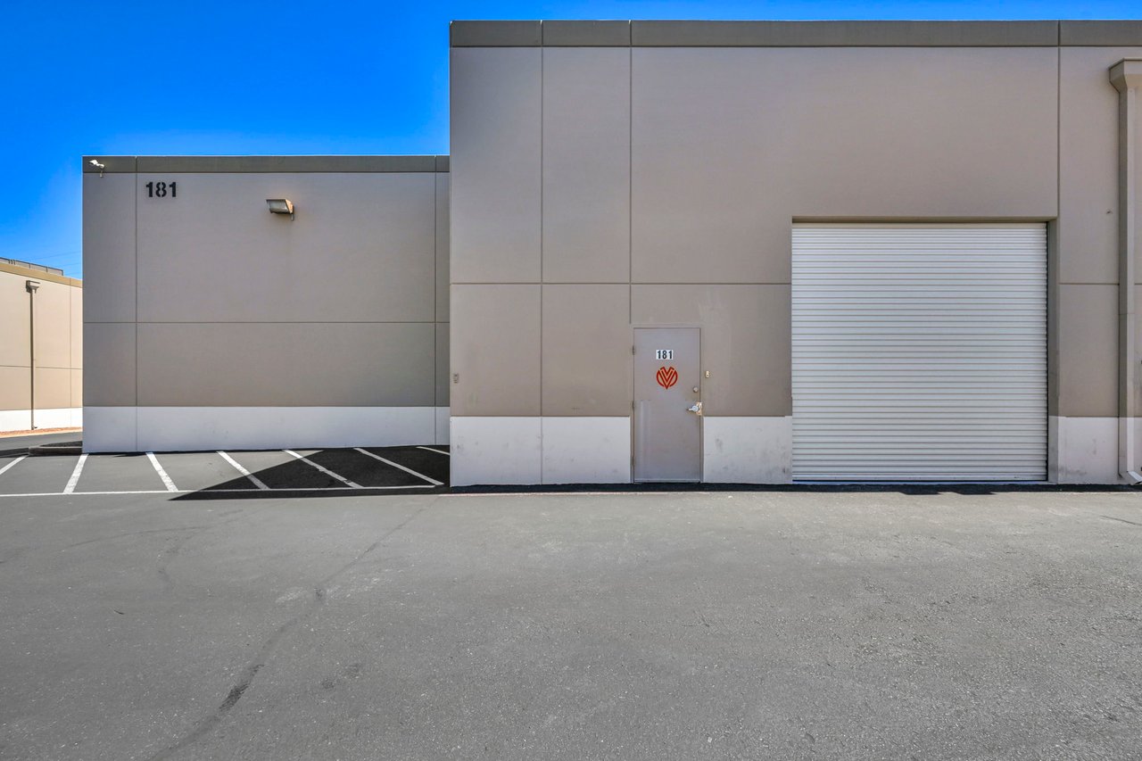 Commercial building exterior marked 181, with a roll-up garage door and striped parking spaces.
