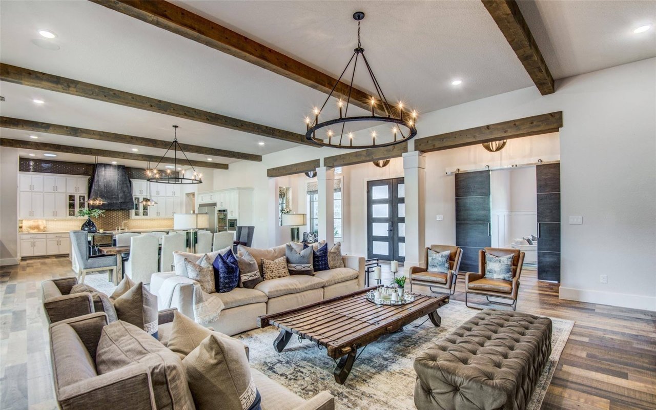 Open-plan living room with exposed wood beams, a circular chandelier, and a rustic coffee table.