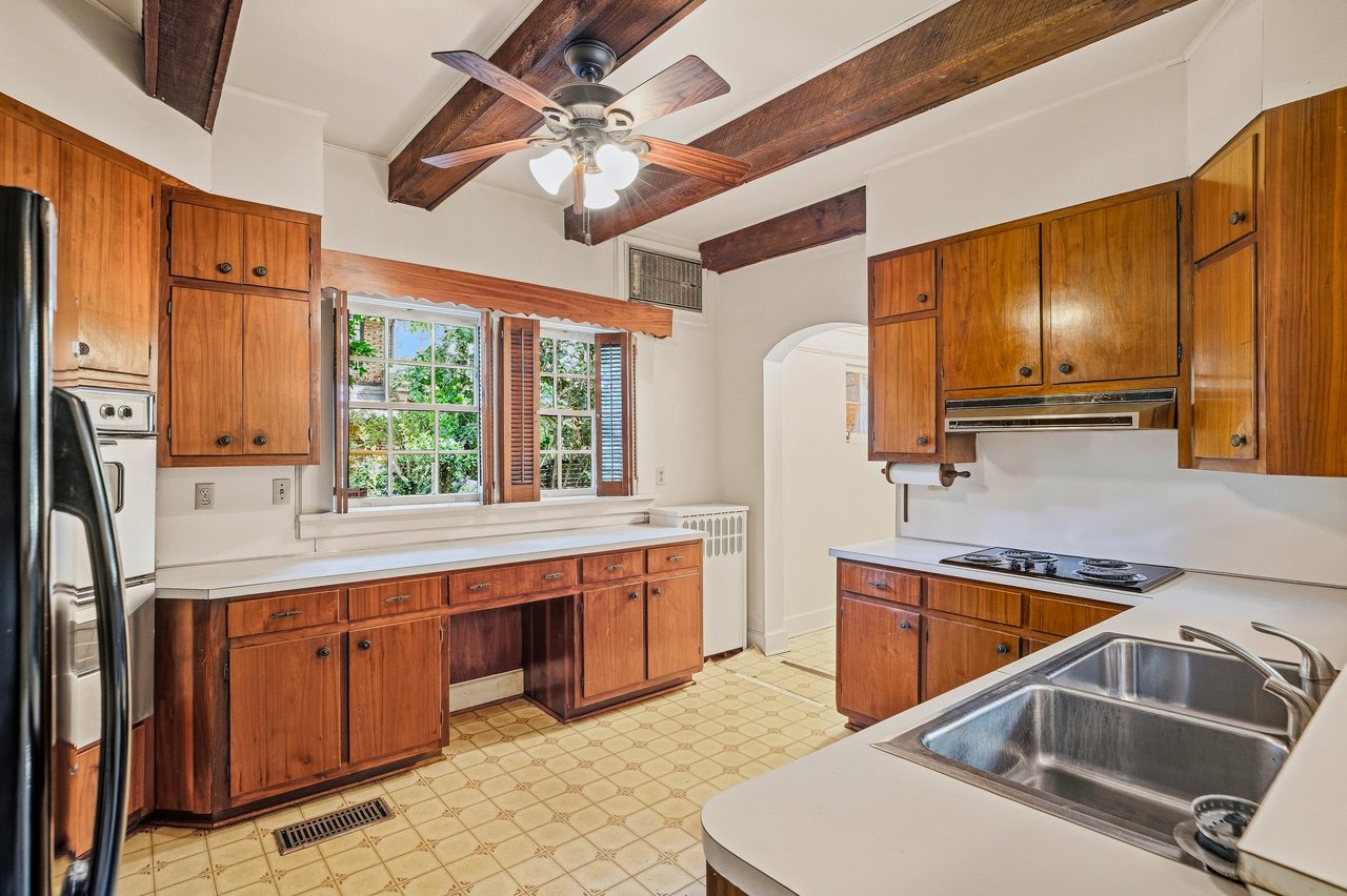 Kitchen with warm wood cabinets, exposed ceiling beams, and a stainless-steel double sink.