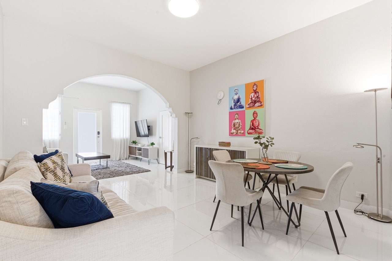 Furnished living and dining room with a cream sofa, round table, and arched opening to a sitting area.