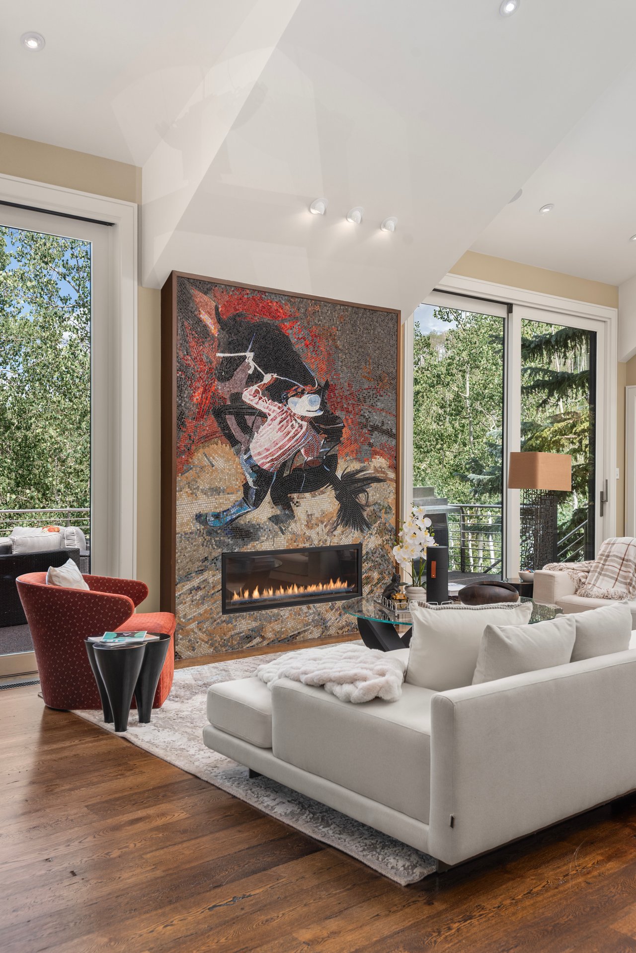 Living room with a mosaic fireplace, white sectional, and large windows overlooking trees.