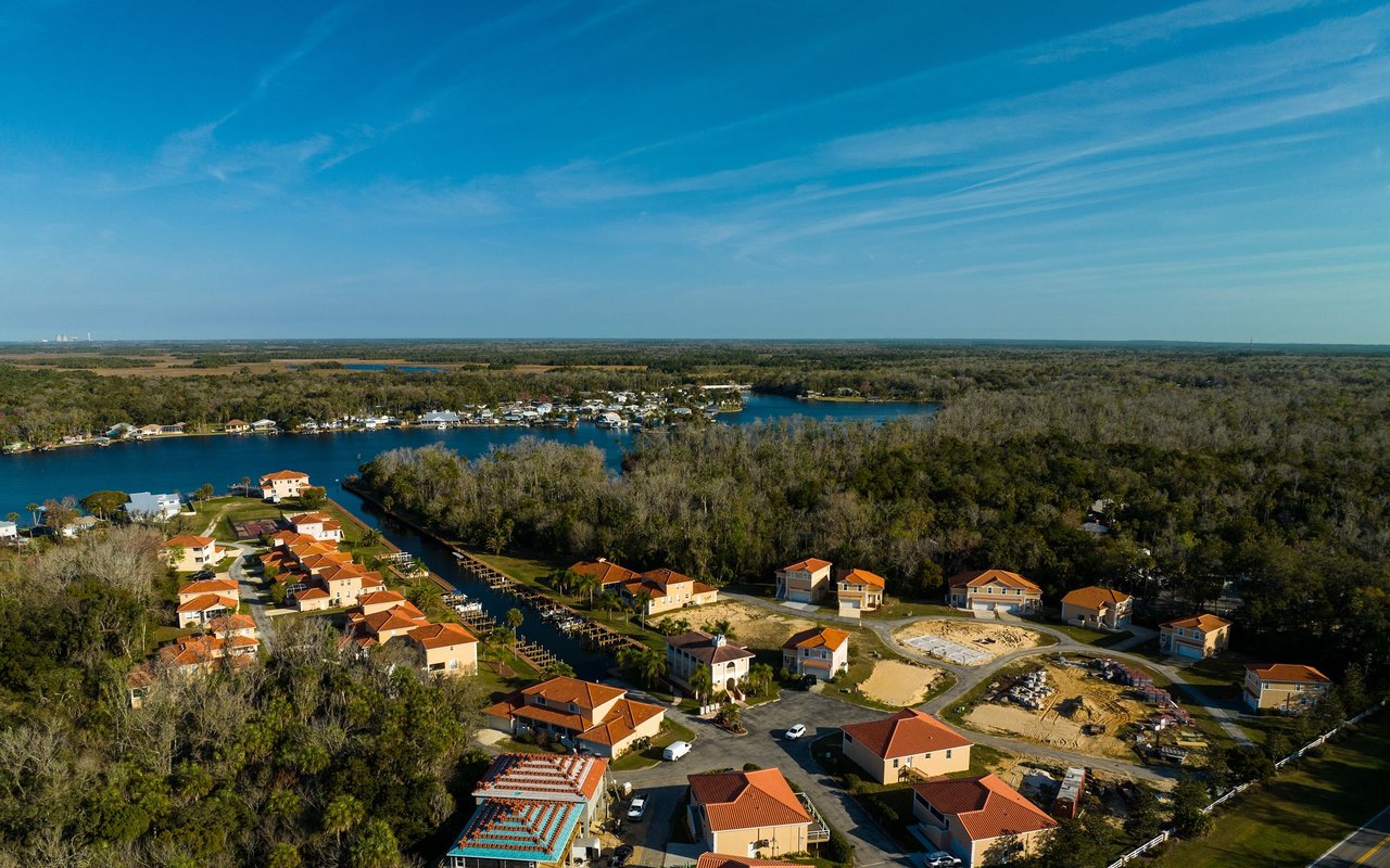 Aerial view of a waterfront neighborhood with canal-front homes and wooded shoreline.