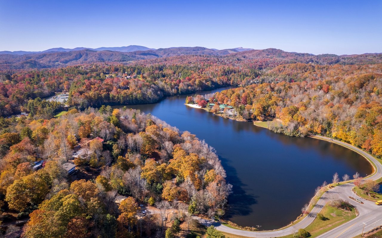 Winding lake amid brilliant fall foliage, scattered homes, and distant mountain ridges.