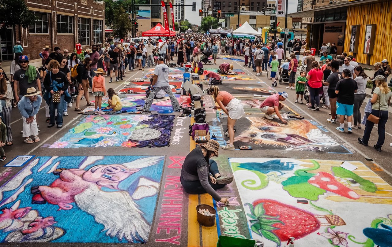 Artists creating colorful chalk murals on city streets during the Denver Chalk Art Festival, showcasing large-scale street paintings in progress.