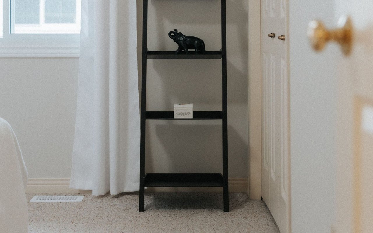 Bedroom corner with black shelving, an elephant figurine, a curtained window, and a white door.