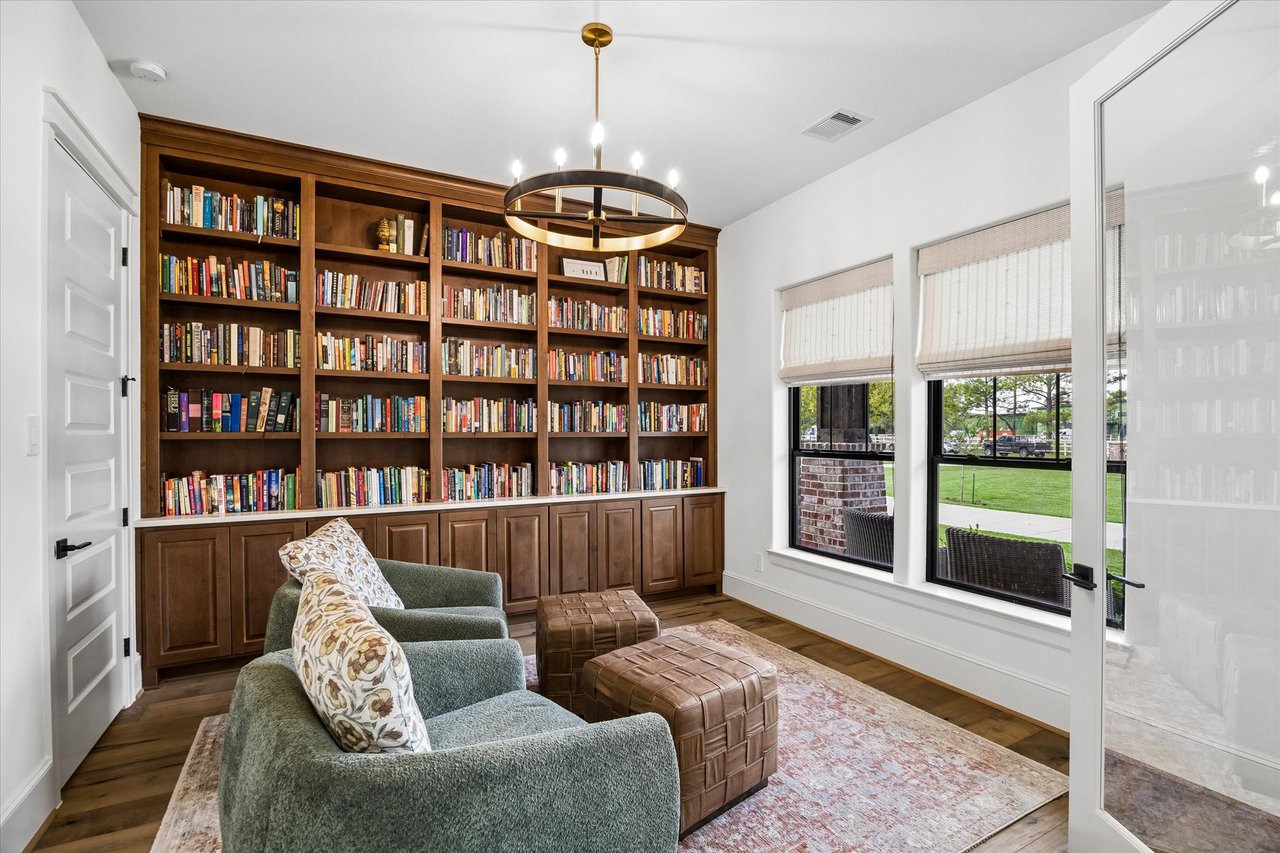 Home library with built-in walnut bookcases, green chairs, and large windows overlooking a lawn.