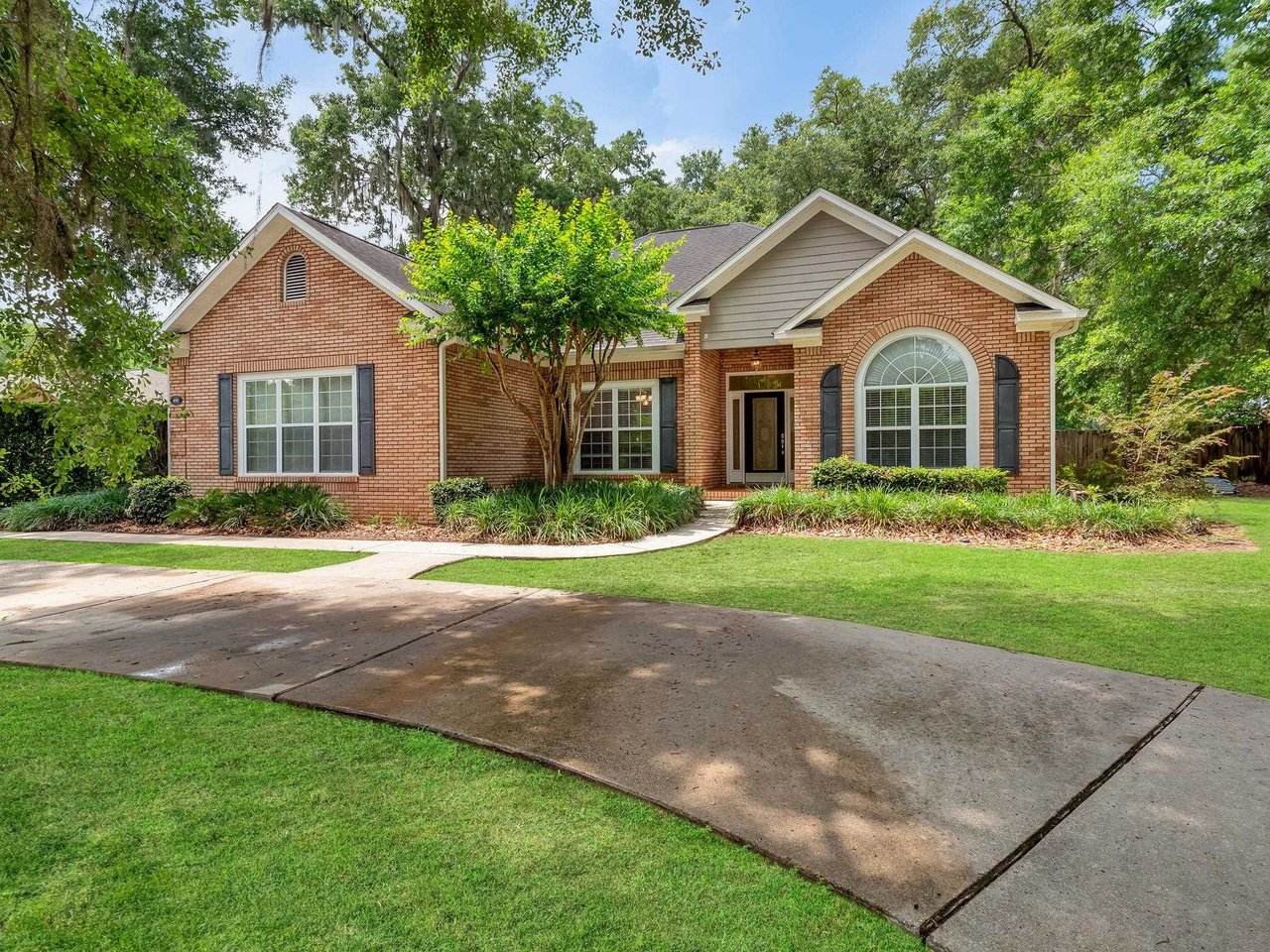 A brick home with a driveway surrounded by lush green grass, showcasing a well-maintained exterior.