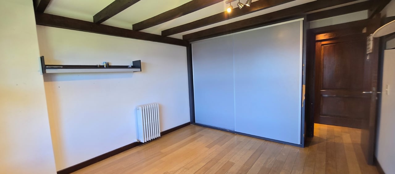 Empty room with exposed ceiling beams, wood flooring, and a built-in sliding-door wardrobe.