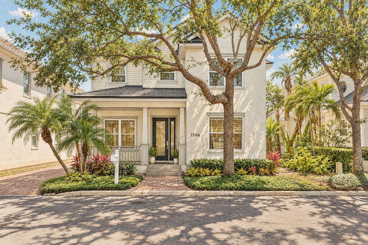 Two-story white home with a covered porch, mature shade tree, and landscaped front garden.