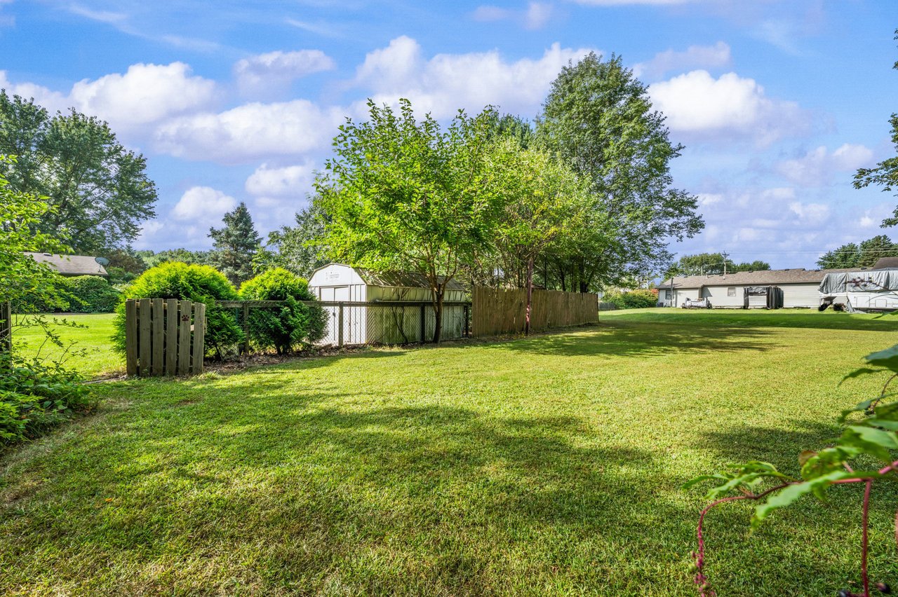 Backyard lawn with mature trees, wooden fencing, and a white storage shed.