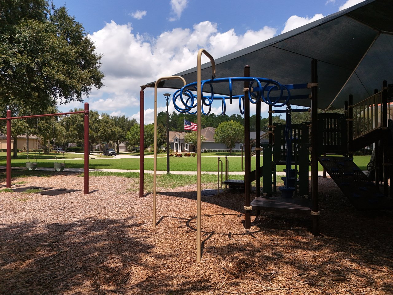 Neighborhood playground with swings and a shaded climbing structure beside a grassy lawn.