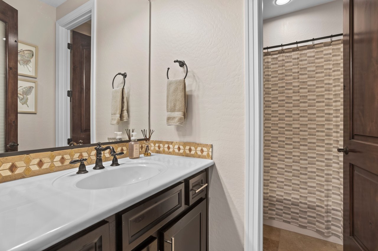 Bathroom with dark wood vanity, white sink, large mirror, and shower with striped curtain.