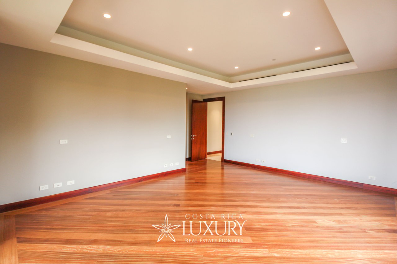 Empty apartment room with polished wood floors, pale walls, and a recessed tray ceiling.