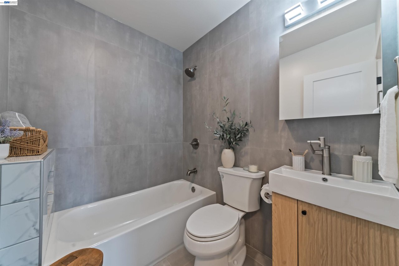 Modern bathroom with gray tile, a white tub, and a wood-front vanity beneath a skylight.