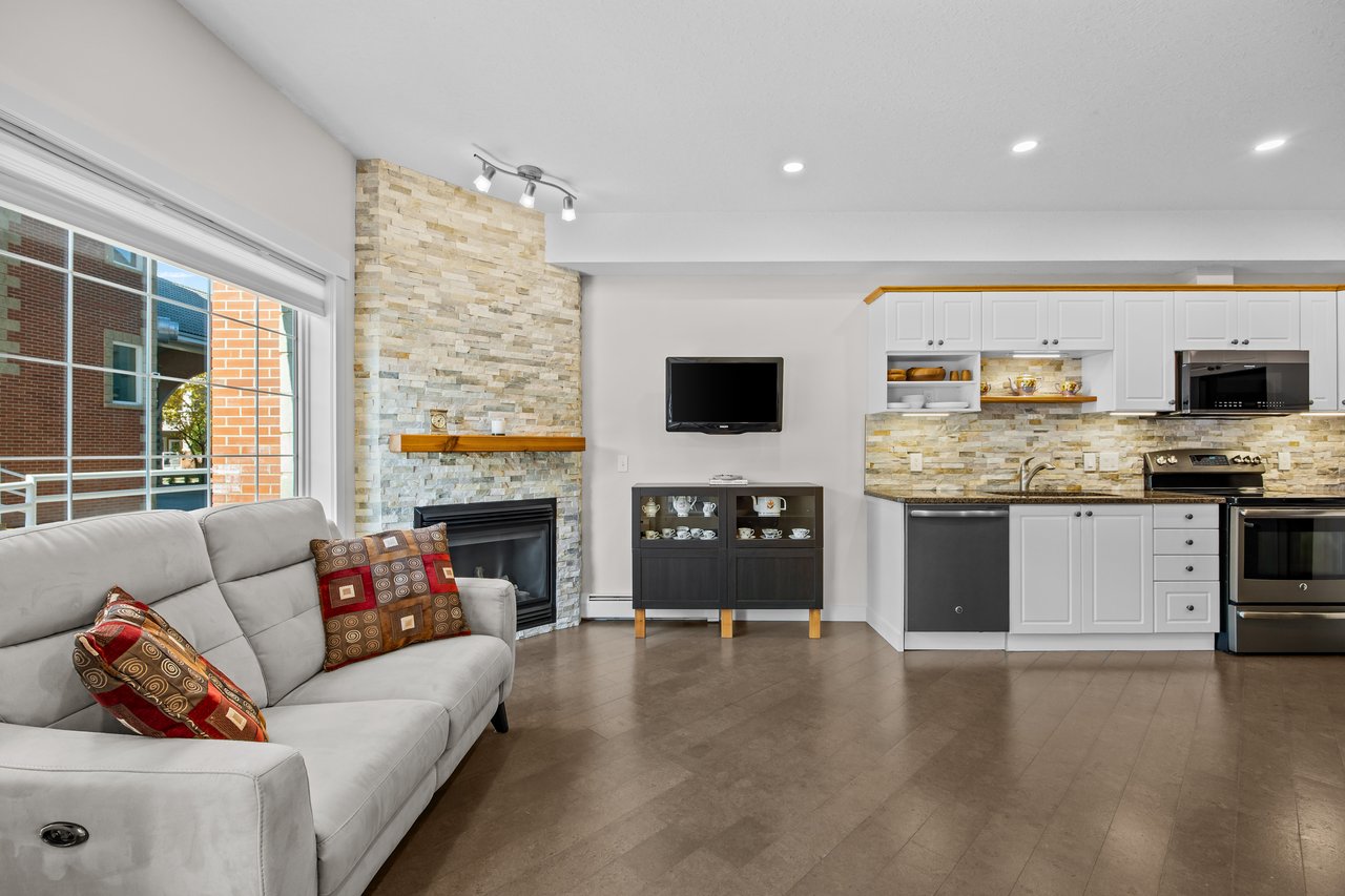 Open living room and kitchen with a stone fireplace, gray sofa, and white cabinetry.