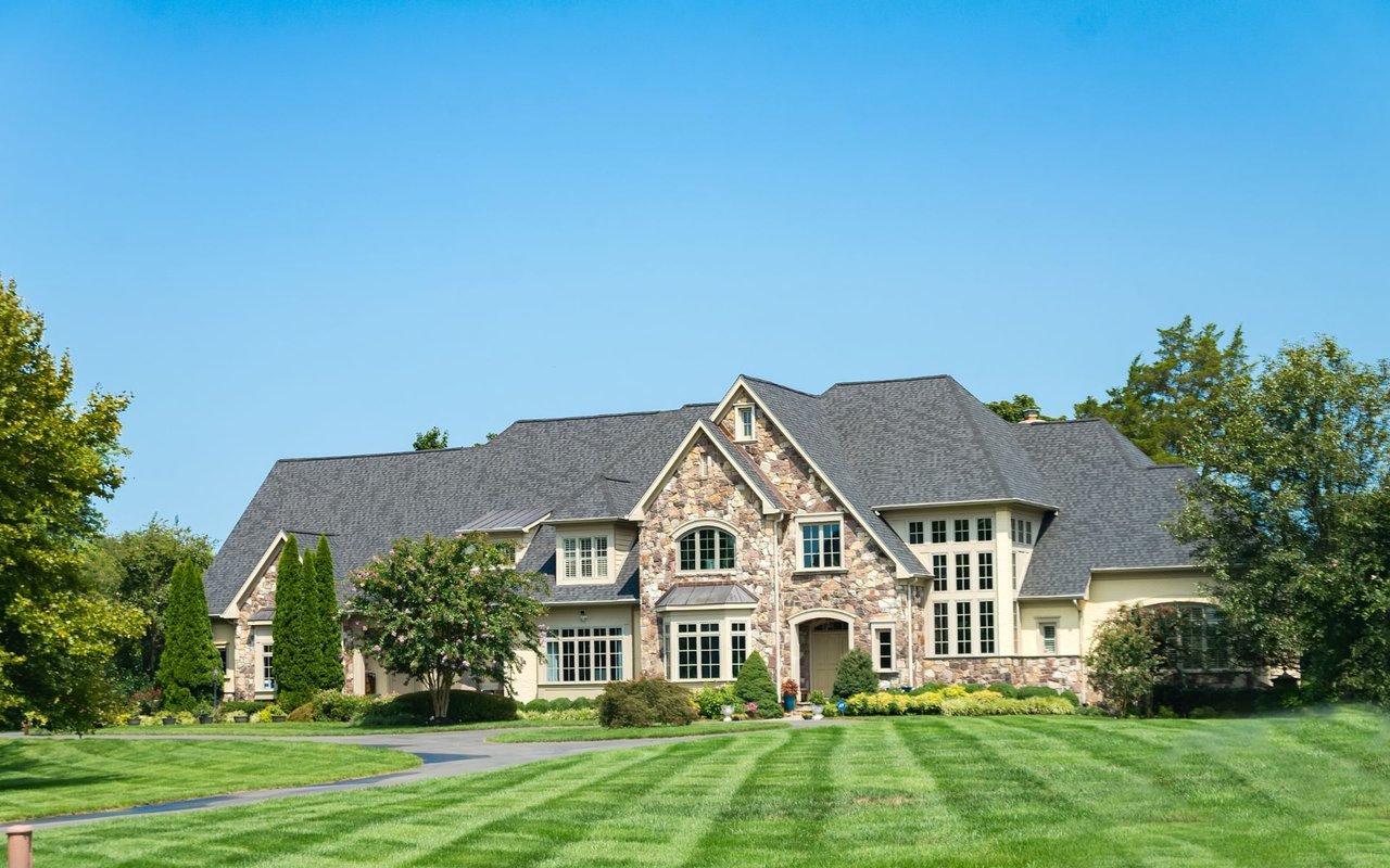 Large stone-and-cream home with a multi-gabled roof and broad striped lawn.