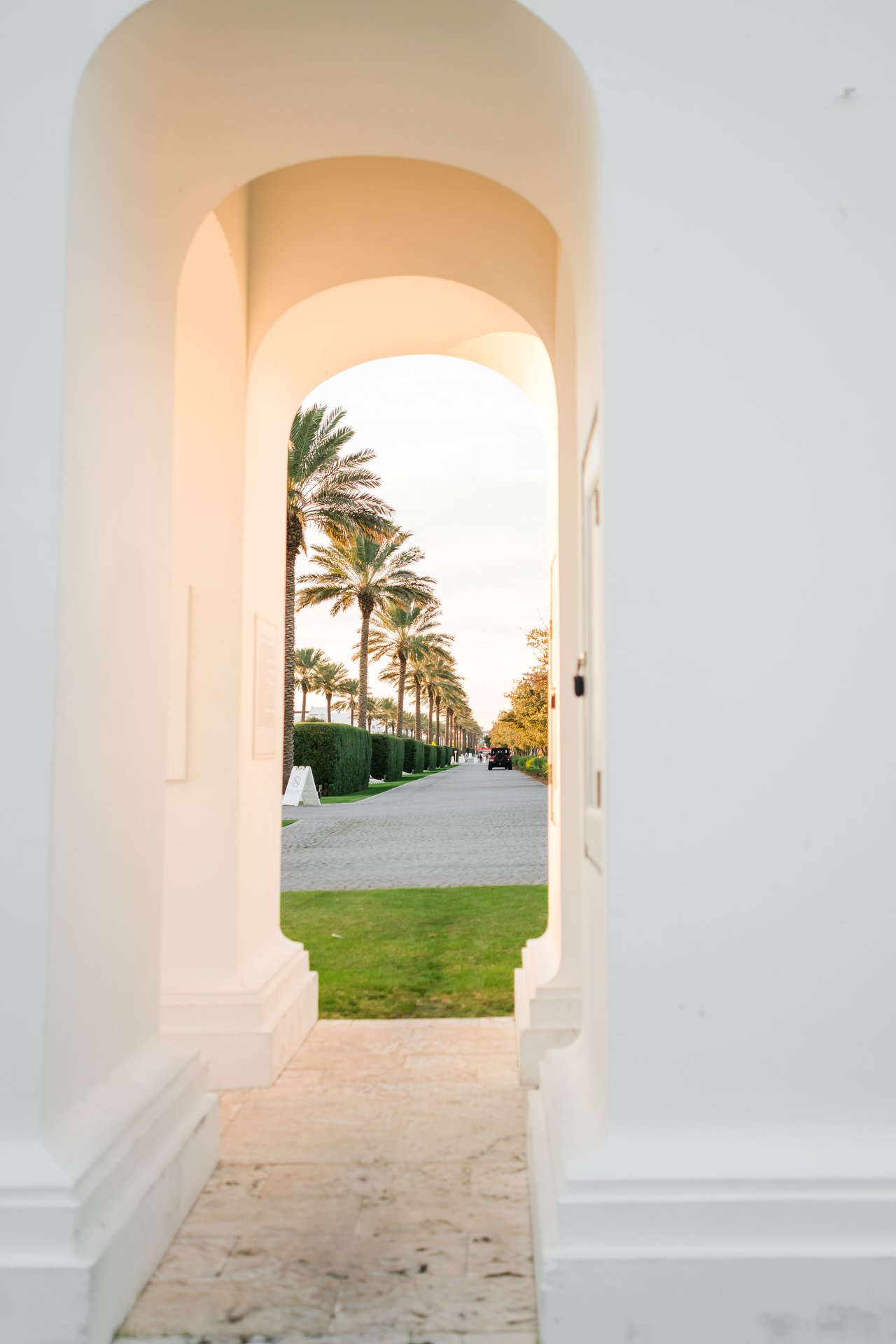 Sunlit all-white barrel-vaulted breezeway arch framing a palm-lined walkway in Alys Beach on 30A, Florida
