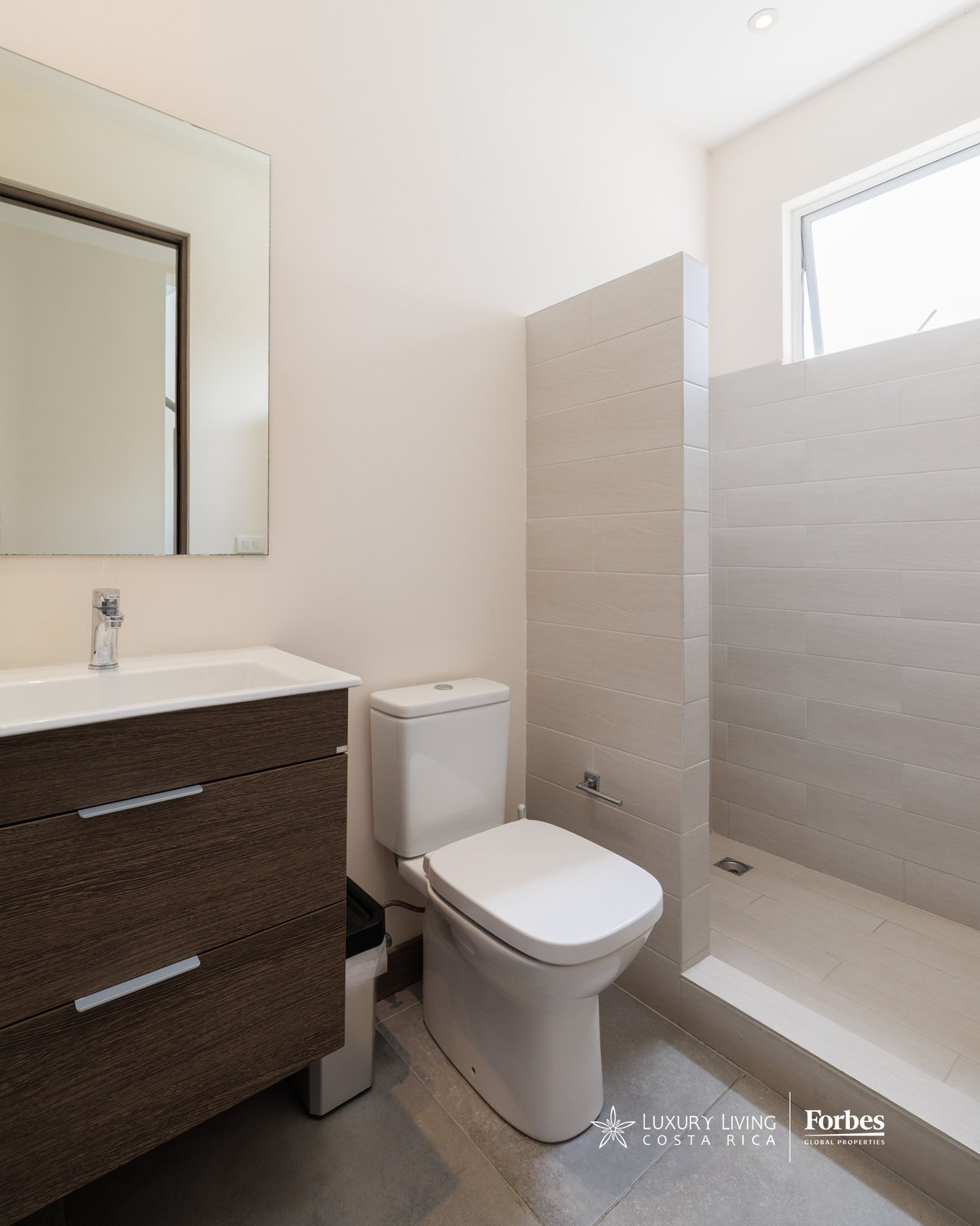 Modern bathroom with a dark wood vanity, white toilet, and tiled walk-in shower.