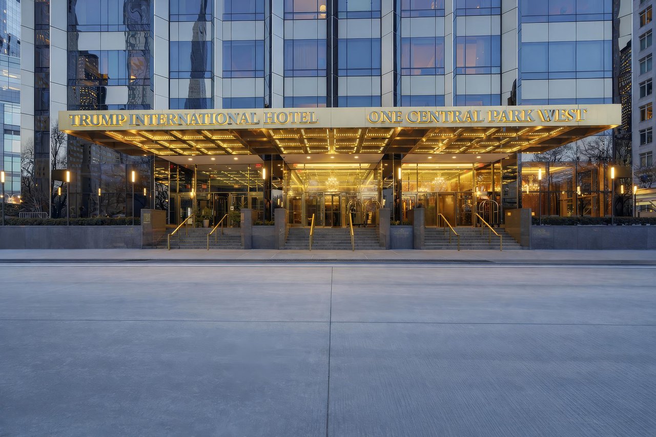 Trump International Hotel entrance beneath an illuminated, gold-lettered canopy at dusk.