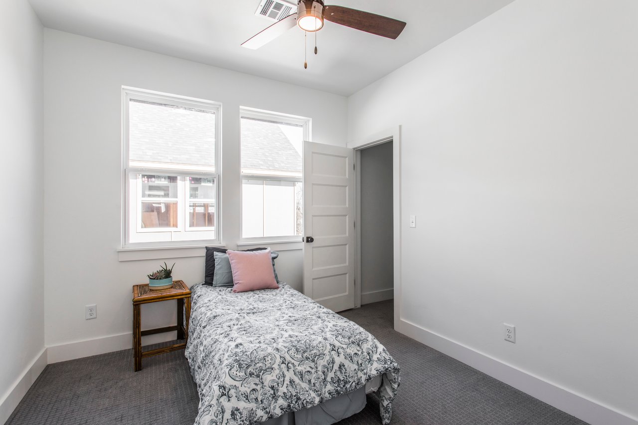 Bedroom with a floral-covered single bed, two windows, and a ceiling fan.