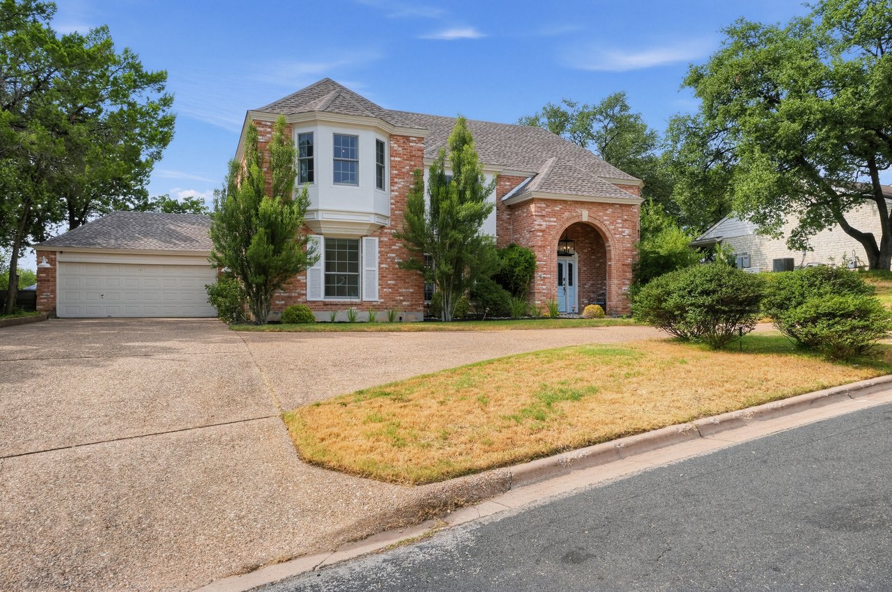 Two-story red brick house with an arched entry, double garage, and mature trees.