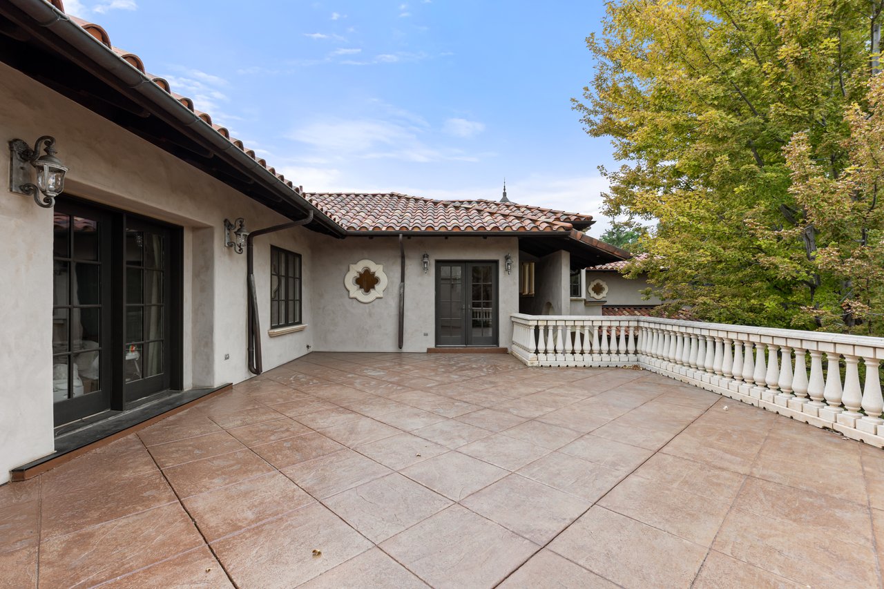 Spacious tiled terrace with a white balustrade, dark-framed doors, and autumn trees.