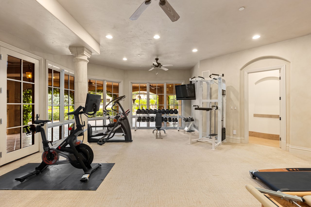 Home gym with a Peloton bike, weight racks, and large windows overlooking greenery.