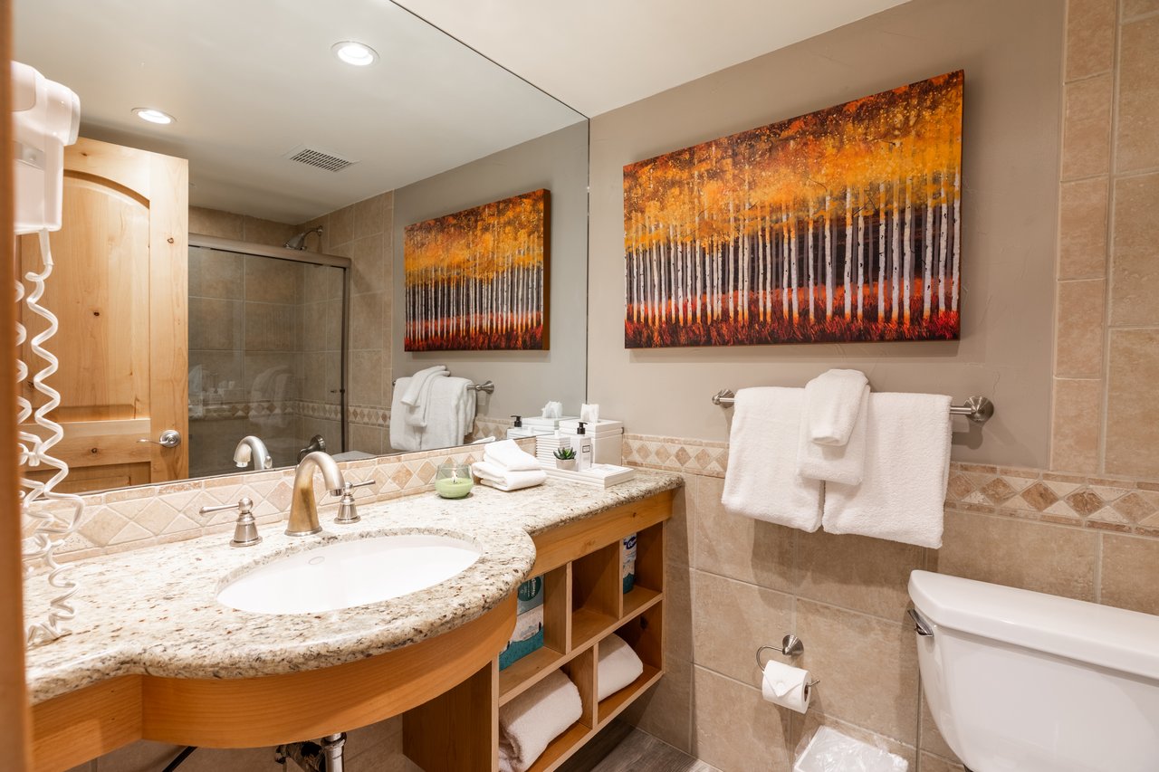 Bathroom with a curved granite vanity, tiled shower, and orange tree artwork.