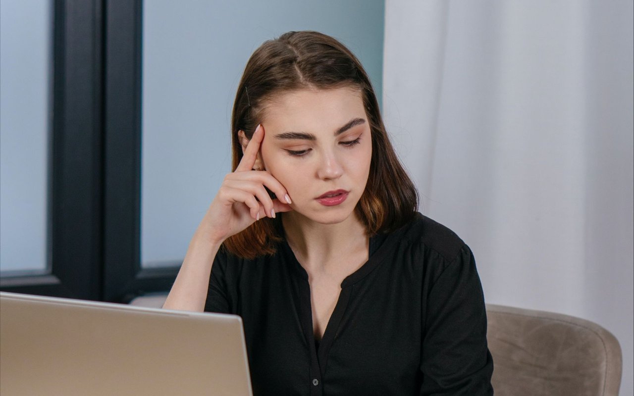 Woman looking thoughtfully at a laptop with her finger against her temple.