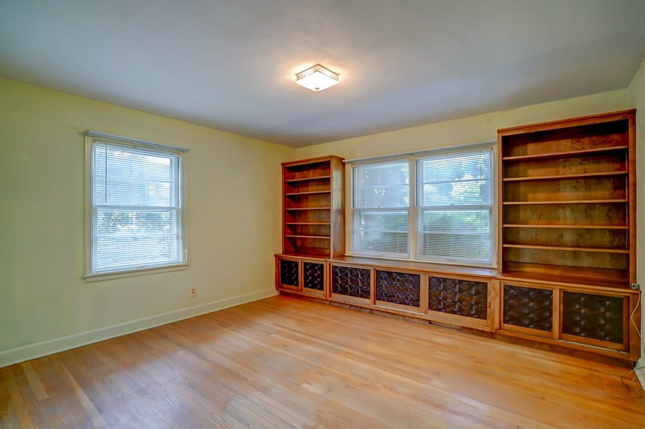 Vacant room with hardwood floors and built-in wooden bookshelves beneath wide windows.