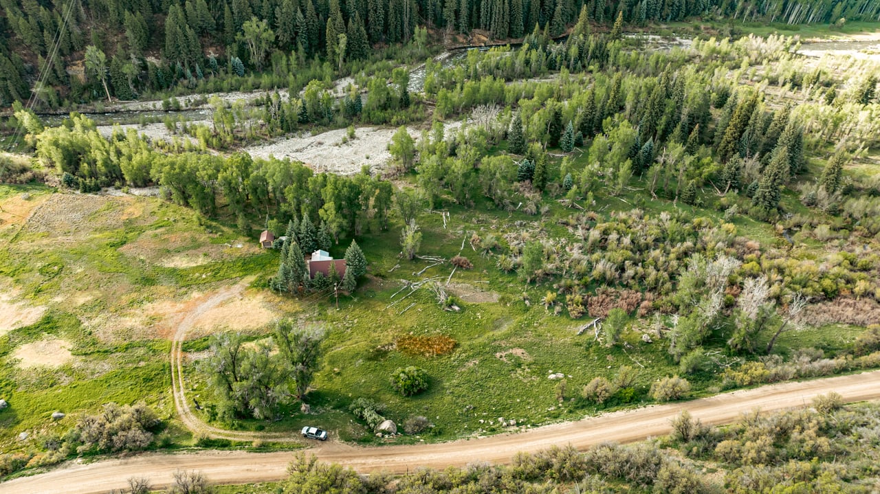 Aerial view of a rural property with scattered buildings, open meadows, a dirt road, and a stream.