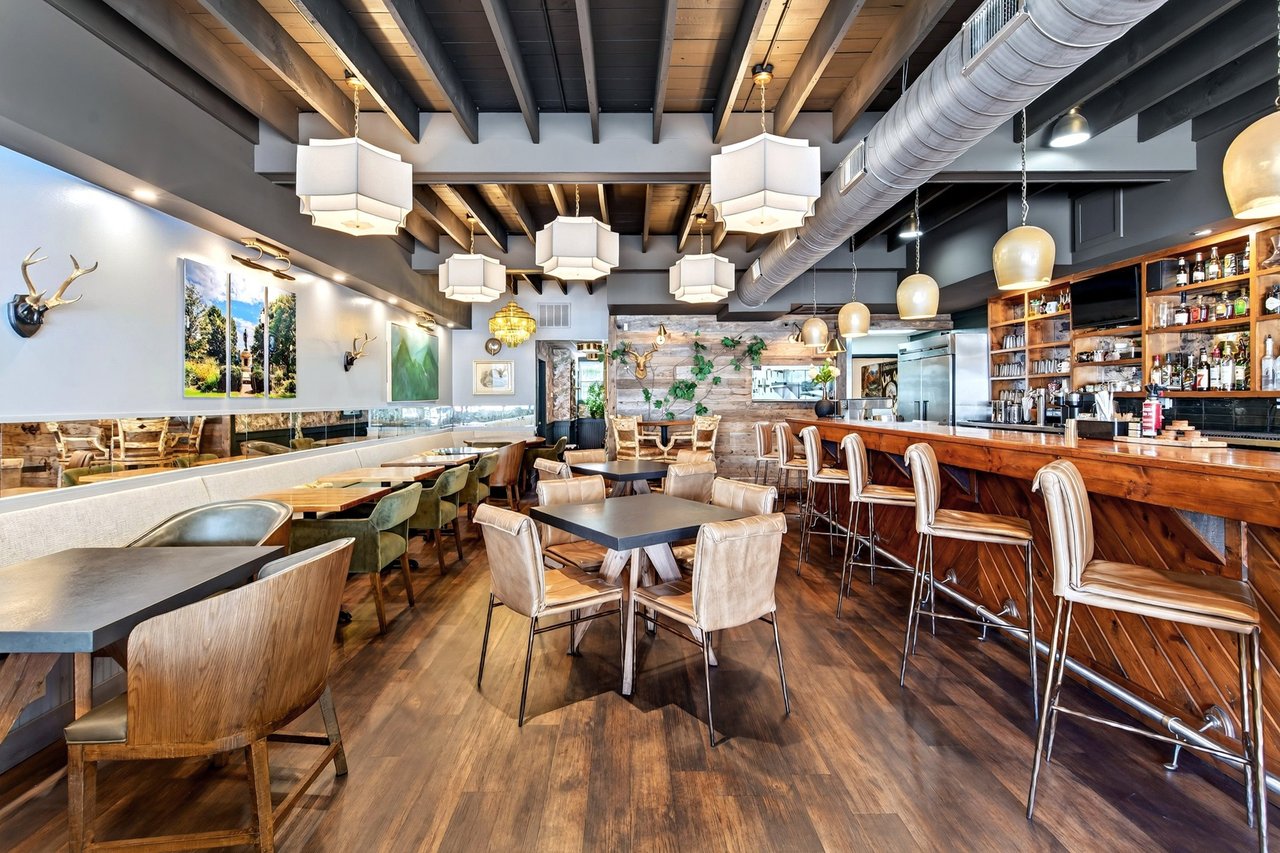 Restaurant dining room with a long wooden bar, exposed ceiling beams, and pendant lights.