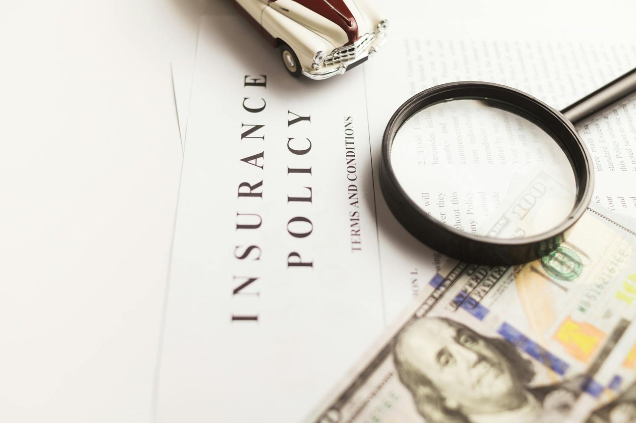 Insurance policy with a magnifying glass, U.S. dollar bills, and a small vintage toy car.