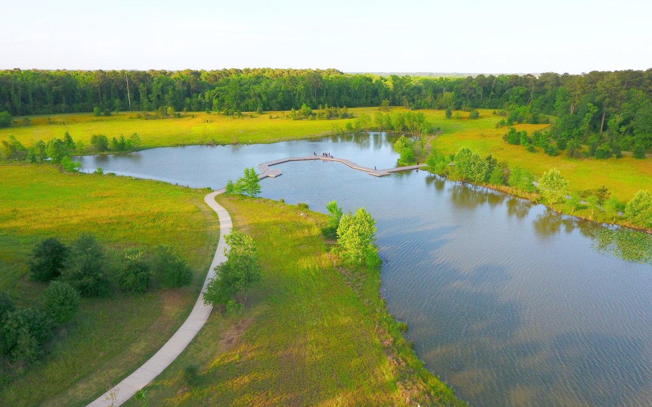 Aerial view of a lake and boardwalk surrounded by grassy parkland and trees.