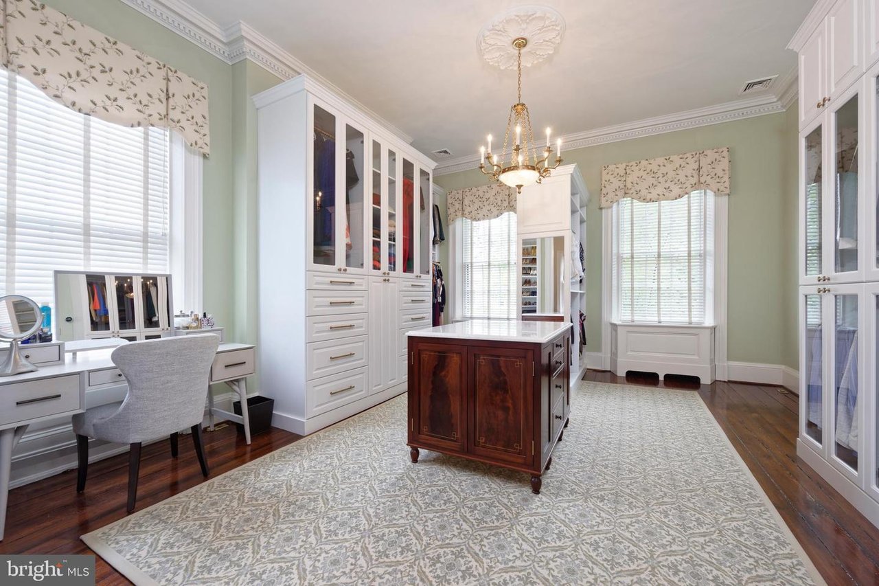 Dressing room with glass-front wardrobes, a dark wood island, vanity, and large windows.