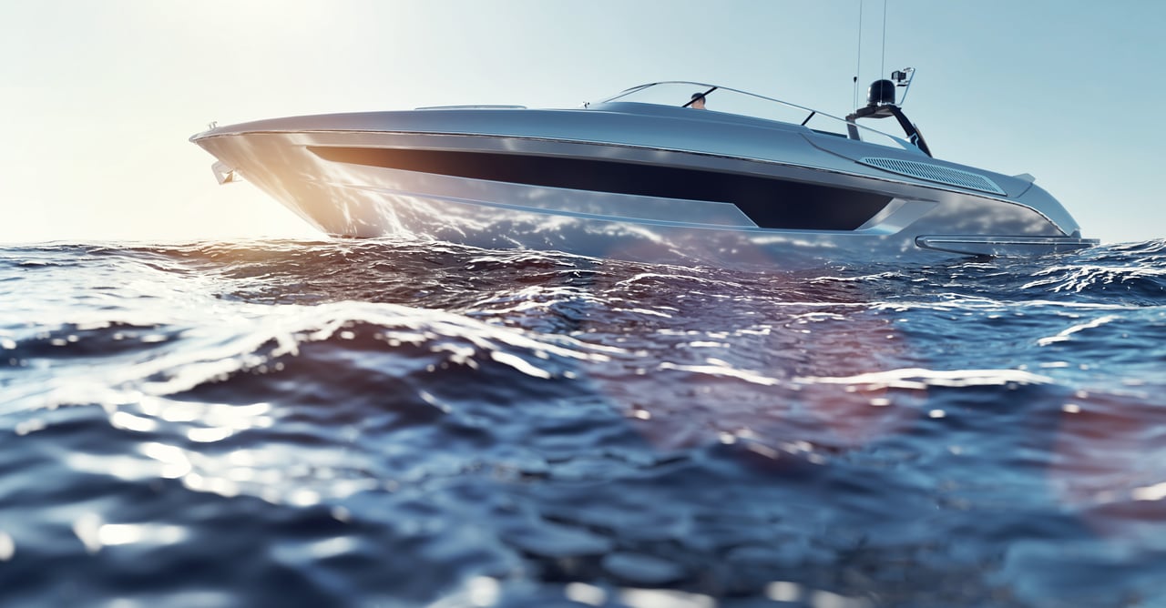 A sleek, silver luxury motor yacht cruising at high speed through deep blue ocean water under a bright sun.