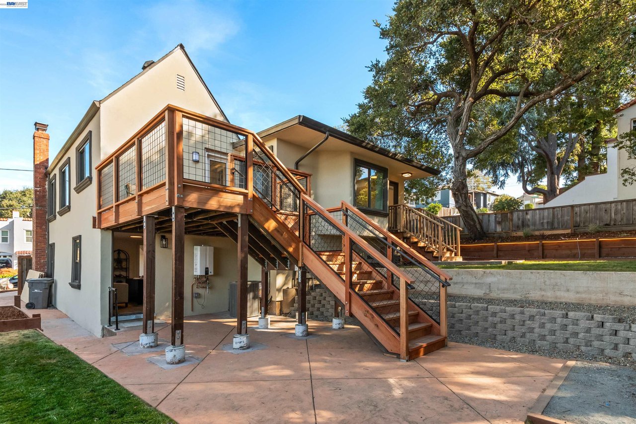 Home’s rear exterior with a raised wooden deck, long staircase, and mature tree in the backyard.
