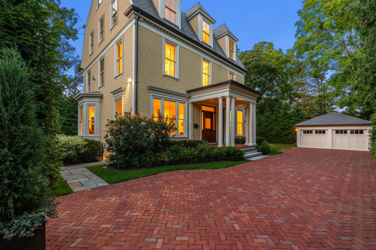 Victorian house with a columned porch and red brick driveway leading to a detached garage.