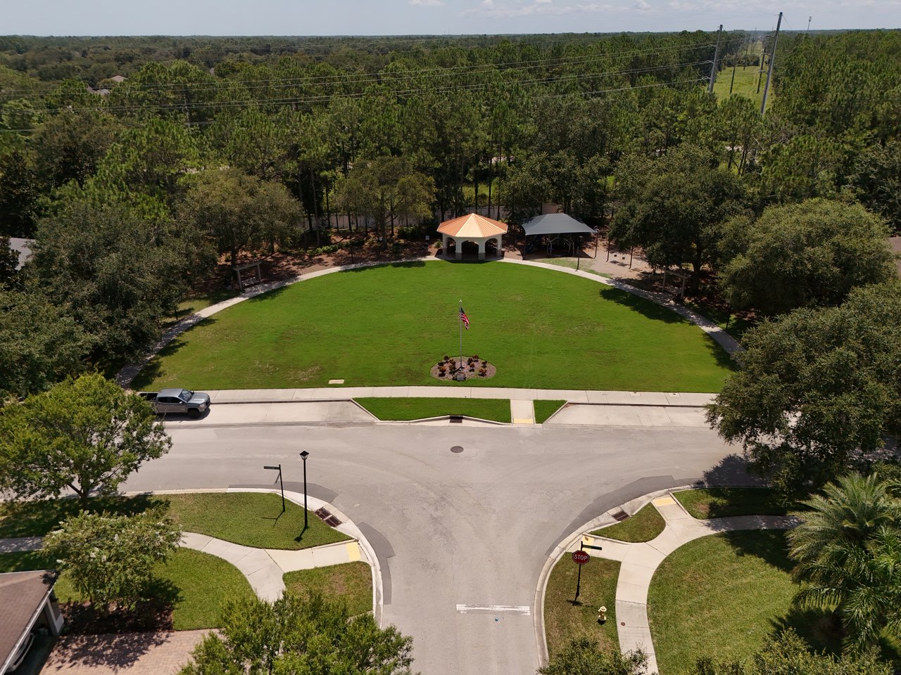 Neighborhood park with a broad lawn, central flagpole, and two covered shelters, viewed from above.