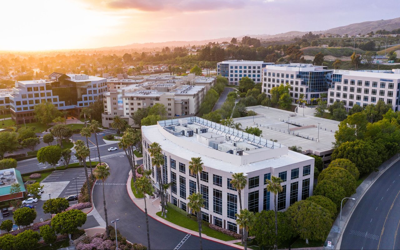 Office park with modern buildings and palm-lined roads, viewed from above at sunset.